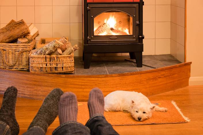 two pairs of feet in front of a roaring fire while a dog sleeps next to it